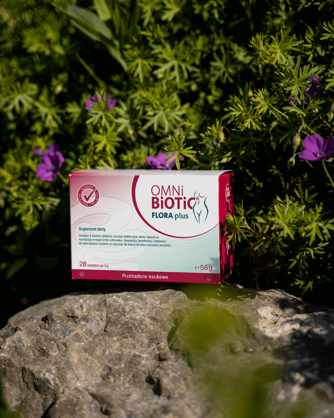 Probiotyk OMNi-BiOTiC Flora Plus trzymany w ręku na tle miasta